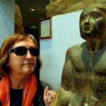 Mara wearing sunglasses looking at statue of seated scribe