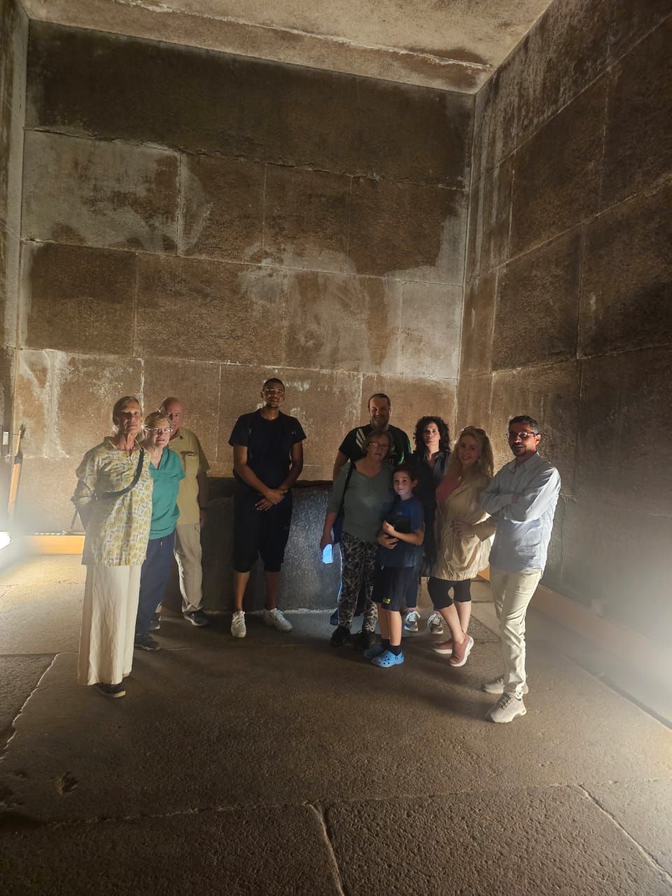 A small group of people standing in front of the sarcophagus in the dimly lit Kings Chamber of the Gt. Pyramid at Giza