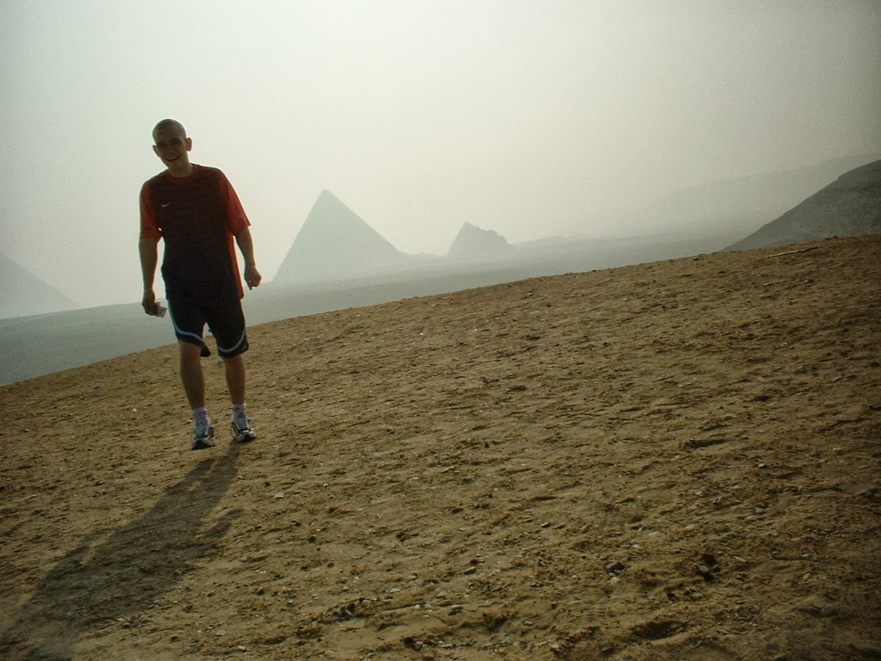 a lone firute of a young man on the deserted Giza Plateau with the three pyramids shrouded in mist at his back in the distance.