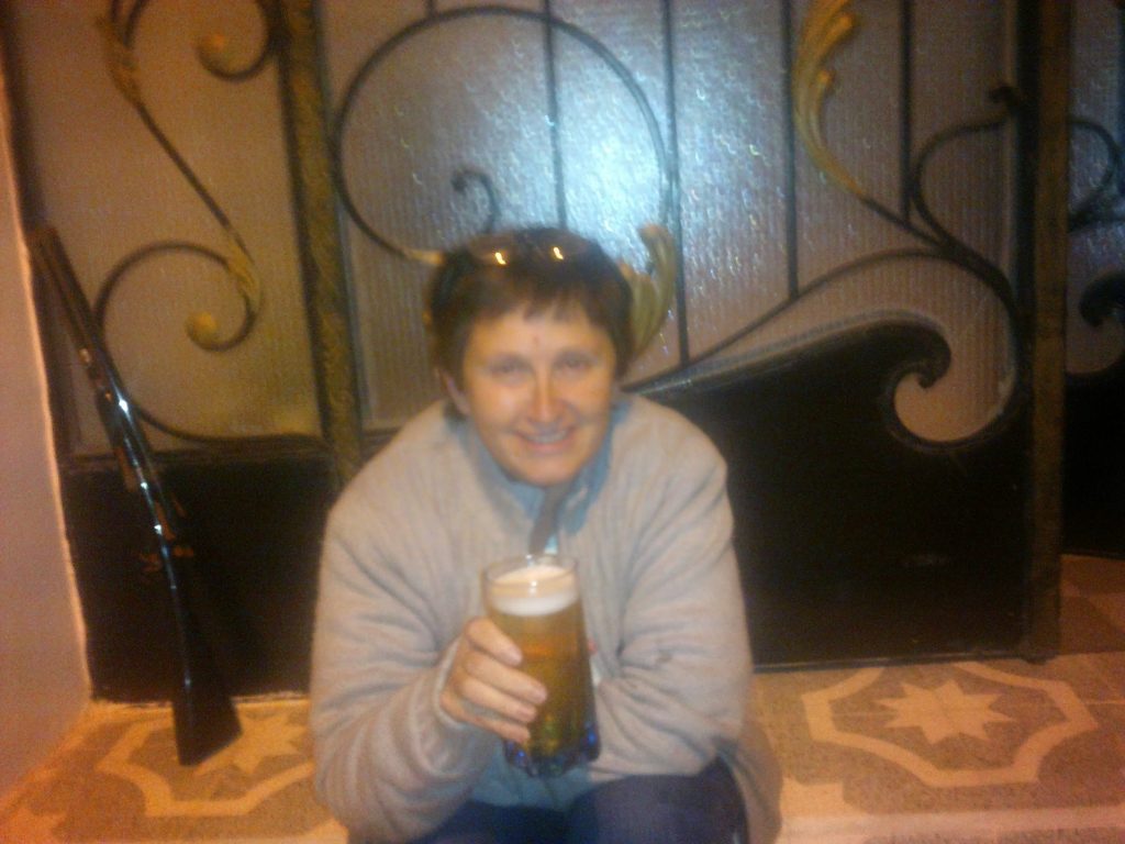 woman sitting on steps outsice decorative wrought iron door, holding a glass of beer