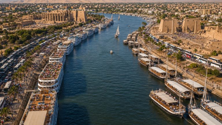 Arial view of Luxor, streets crowded with buses on both sides and the River Nile with boats docked on either side.
