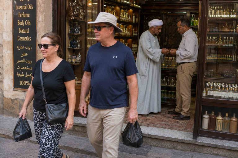 a man and a woman walking out of a perfume shop holding shopping bags. Behind them the shop owner is give another man money