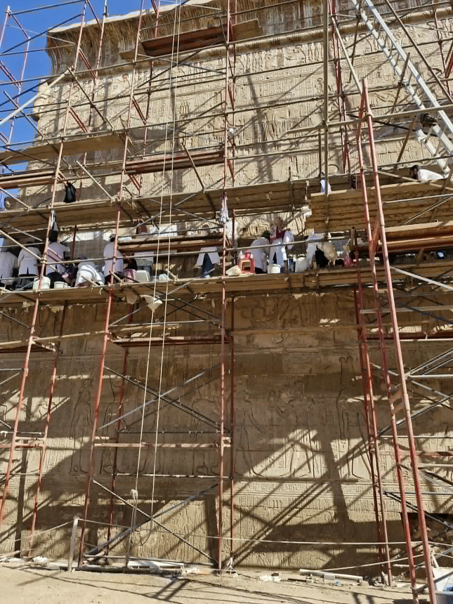 On a high scaffold against the Temple wall a team of white-coated workers are cleaning and restoring the wall