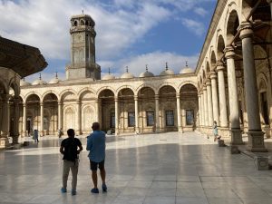 Two men standing in the middle of an open courtyard of a mosque. Courtyard is surrounded by columns