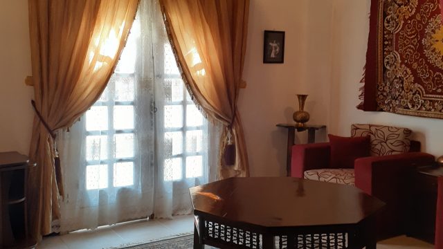 Every suite at Mara House has a separate living room, individually styled - hotel with a difference! living room, two comfortable red armchairs, large red/yellow arabian wall hanging, double doors opening to balcony, large table stands in the centre of room on oriental rug, beige floor tiles. Light & airy ambiance