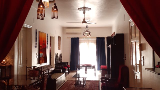 Spacious Living Room in the Exec Suite. Perfect for family or group of friends to relax in private. Living Room in Exec Suite 4 at Mara House Luxor 3m x 14m, two separate seating areas and a dining area. Beige floor tiles and walls adorned with artwork.