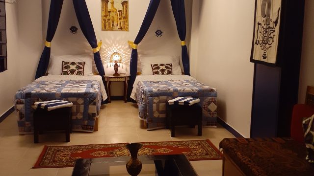 Spacious twin bedroom with comfortable seating area large bedroom, 2 single beds covered with patchwork quilt blue/white. Royal blue canopies over beds, couch, small table and wall decor