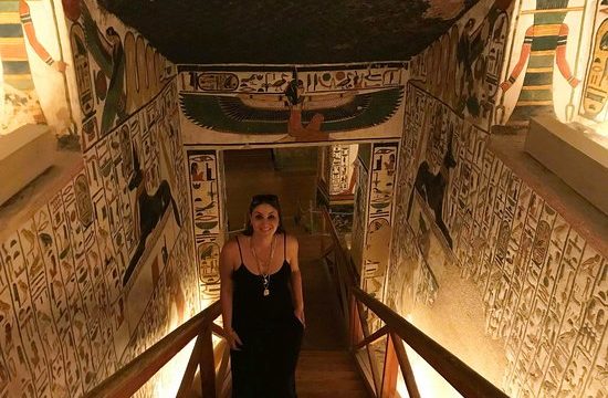 young lady ascending stairway from tomb. Walls on either side and ceiling colourfully decorated with carvings