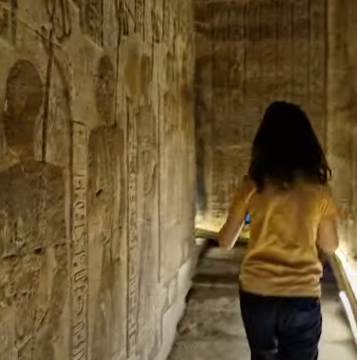 A young boy in a yellow t-Shirt ascending the worn steps of the spiral staircase at Dendera - surrounding walls covered in carvings